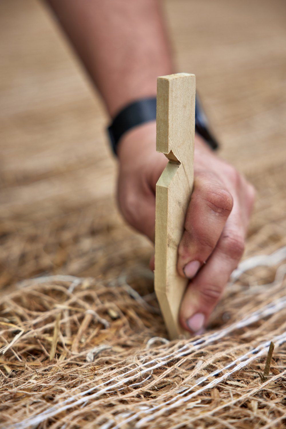 Hand placing an Eco-Peg wood stake into a straw blanket